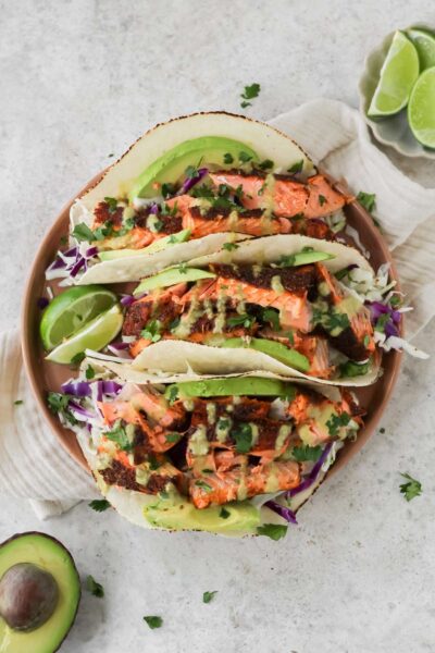 A plate filled with three air fryer salmon tacos and two lime wedges sitting on the plate.