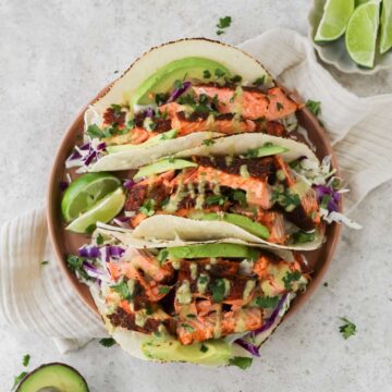 A plate filled with three air fryer salmon tacos and two lime wedges sitting on the plate.