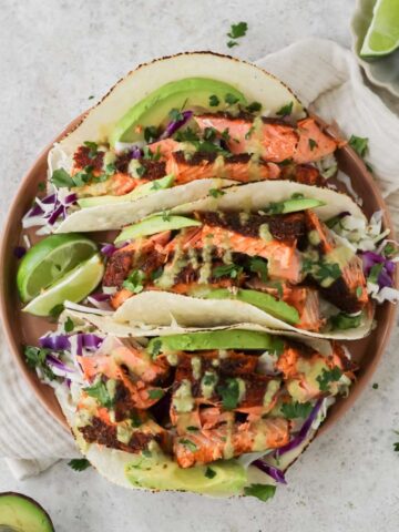 A plate filled with three air fryer salmon tacos and two lime wedges sitting on the plate.