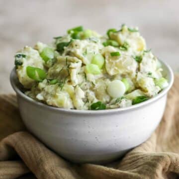 A bowl of potato salad with spring onions sitting on a tan tea towel.