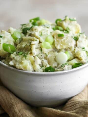 A bowl of potato salad with spring onions sitting on a tan tea towel.