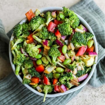 A bowl filled with broccoli and edamame salad sitting on an blue tea towel.