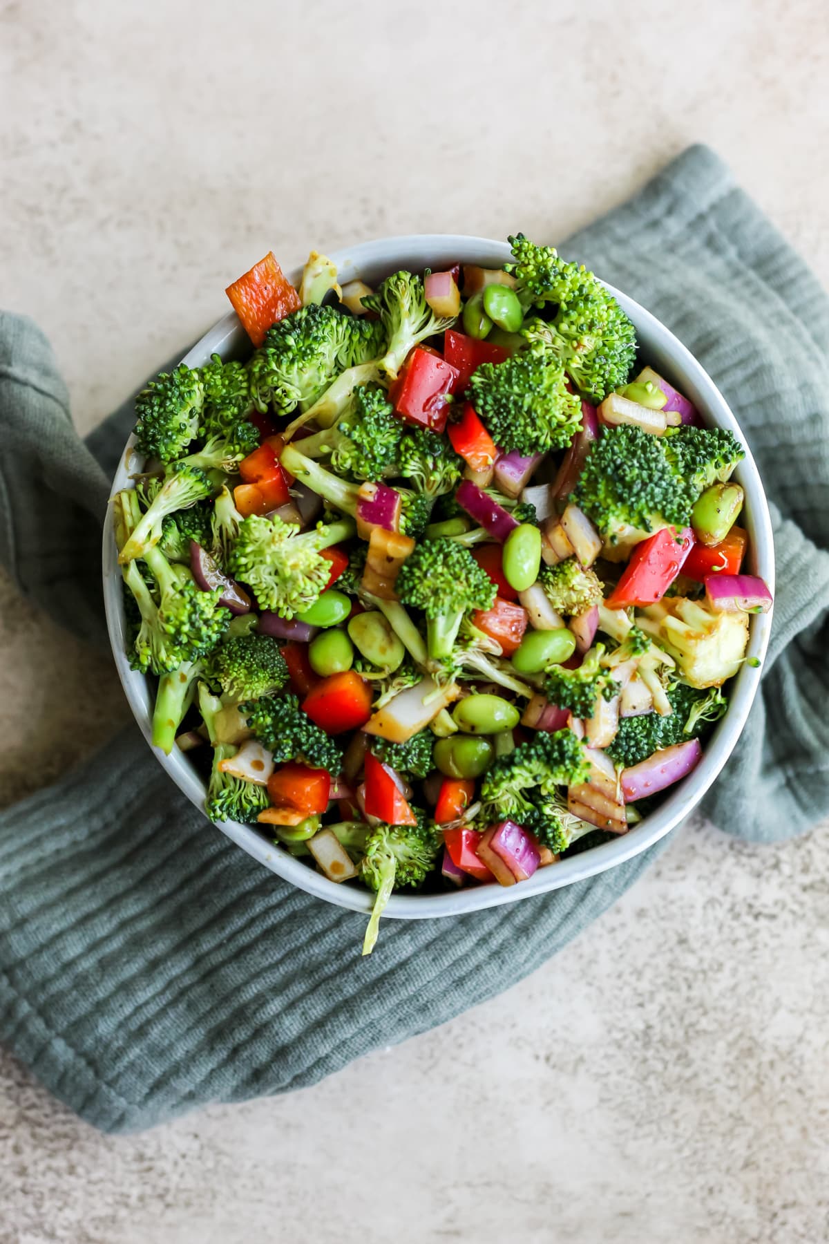 A bowl filled with broccoli and edamame salad sitting on an blue tea towel.