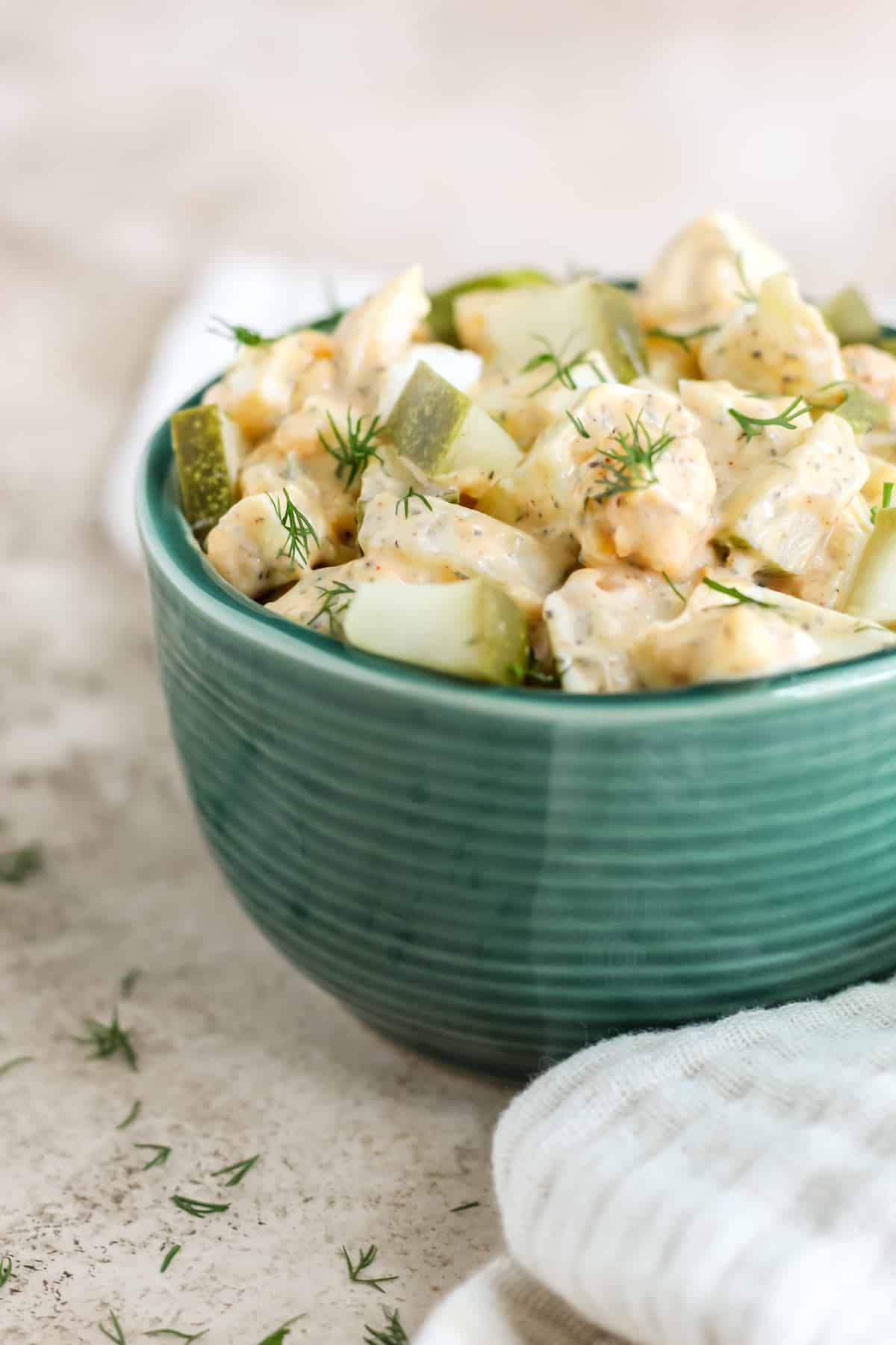 A green bowl on a tan background filled with dill pickle egg salad.