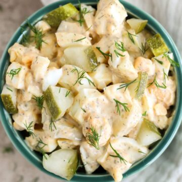 A green bowl on a tan background filled with dill pickle egg salad.