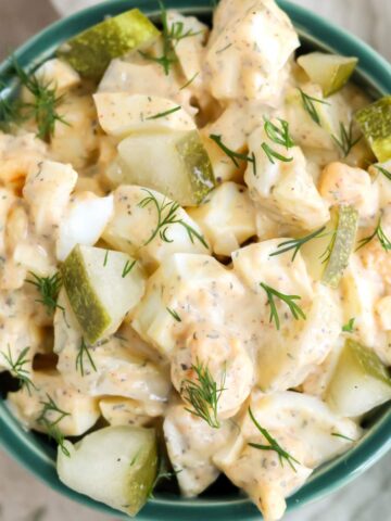 A green bowl on a tan background filled with dill pickle egg salad.