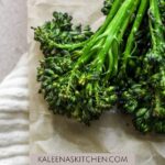 A Pinterest pin with air fryer broccolini sitting on tan parchment paper.
