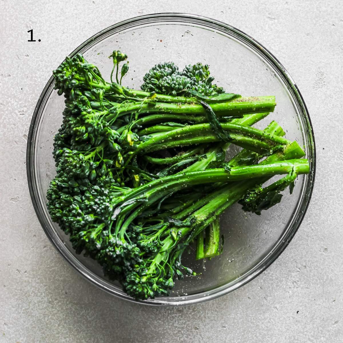 Seasoned broccolini sitting in a glass bowl.