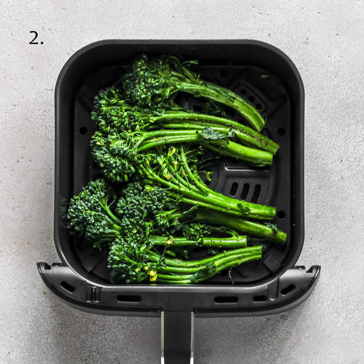 Seasoned broccolini in an air fryer basket.