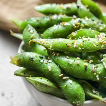 Air fryer edamame in a small bowl with a dark tan tea towel next to the bowl.