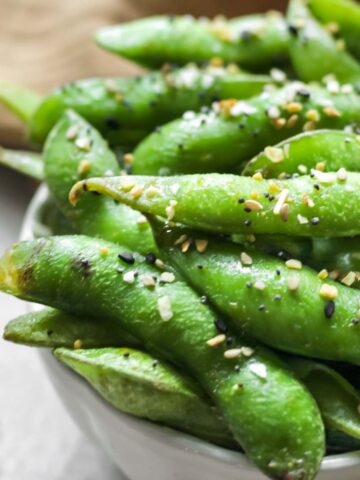 Air fryer edamame in a small bowl with a dark tan tea towel next to the bowl.