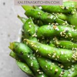 A Pinterest pin with air fryer edamame in a small bowl with a dark tan tea towel next to the bowl.