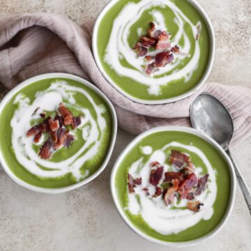 Three bowls of broccolini soup with a white drizzle of coconut milk and a sprinkle of crispy bacon on top.