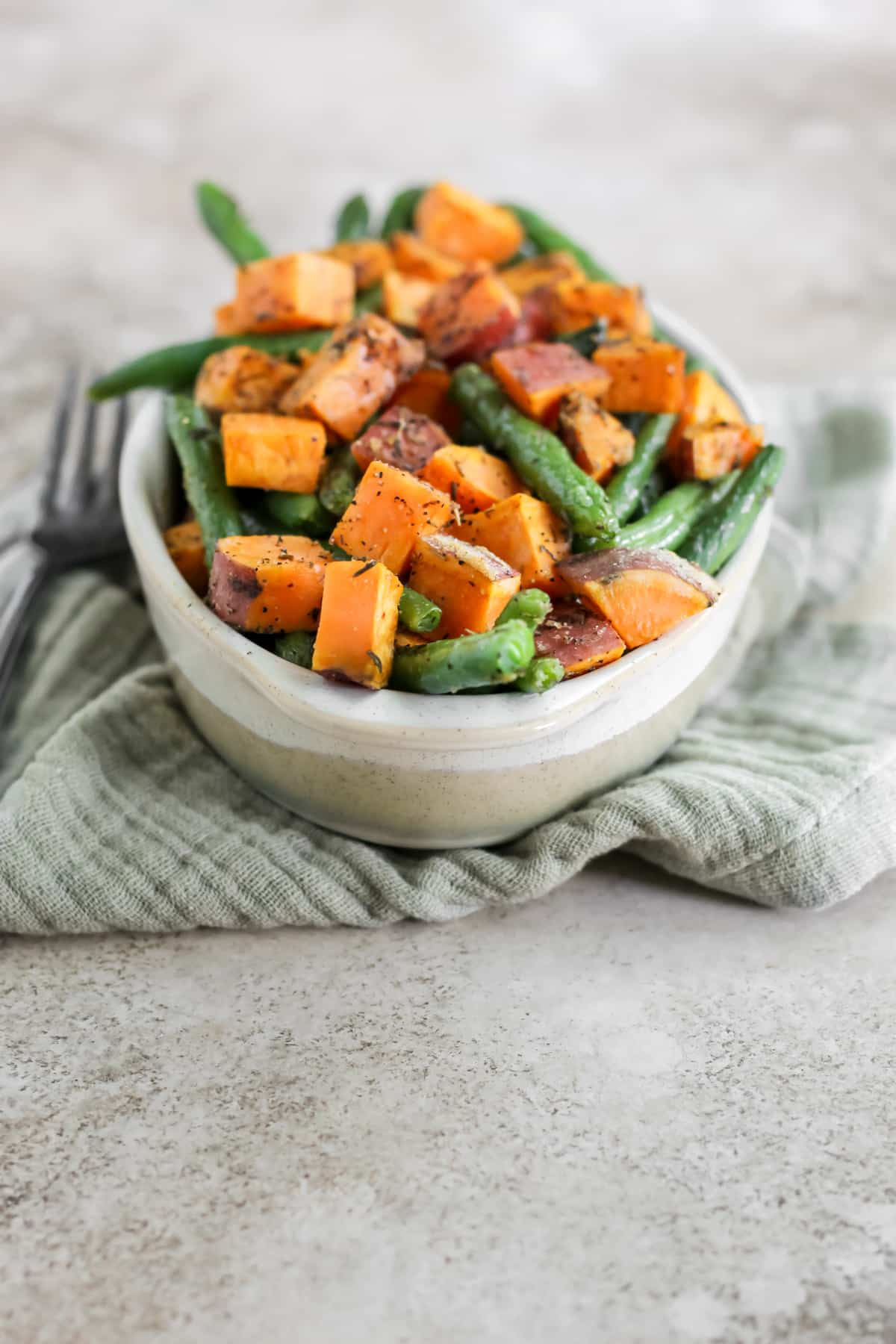 An oval dish filled with roasted sweet potatoes and green beans sitting on a green tea towel.