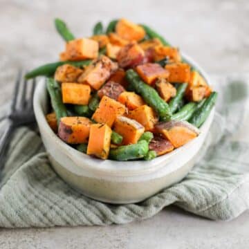 An oval dish filled with roasted sweet potatoes and green beans sitting on a green tea towel.