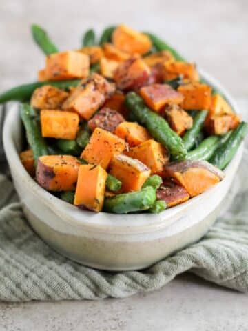 An oval dish filled with roasted sweet potatoes and green beans sitting on a green tea towel.