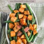 A Pinterest pin with an oval dish filled with roasted sweet potatoes and green beans sitting on a green tea towel.