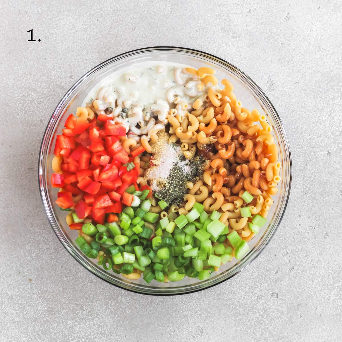 A bowl filled with protein pasta, diced celery, diced red bell pepper, diced green onion, seasoning, ranch, and buffalo sauce.