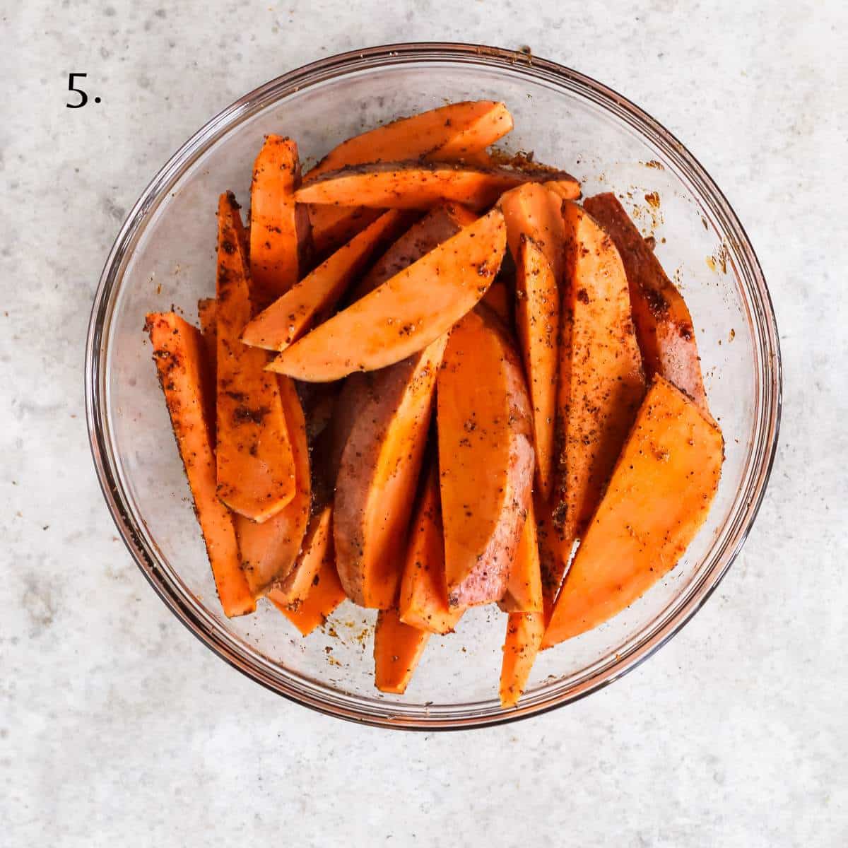 A bowl filled with uncooked sweet potato wedges and seasonings.