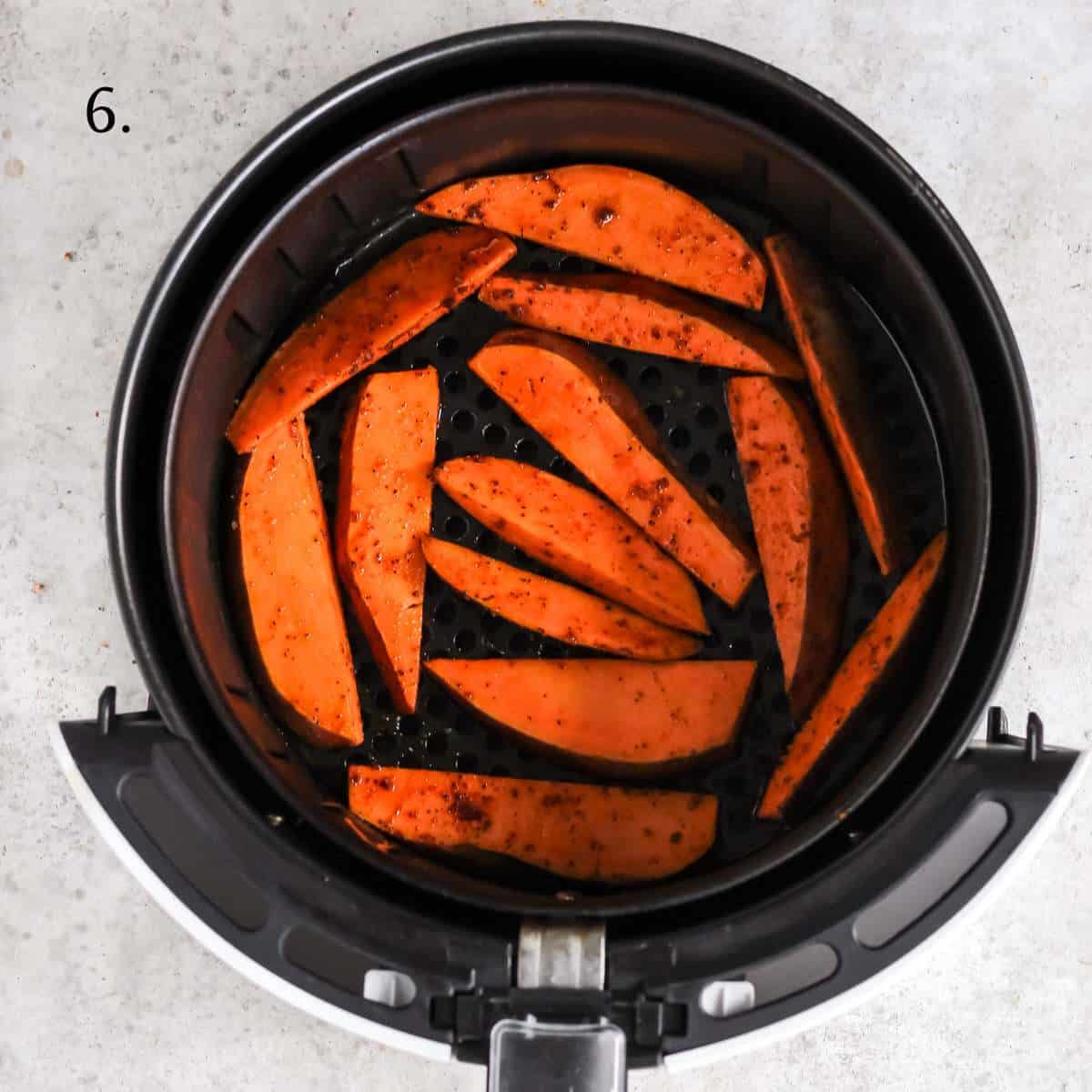 Sweet potato wedges inside the basket of an air fryer.