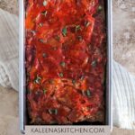 A Pinterest pin with a meatloaf pan filled with Whole30 Meatloaf, sprinkled with fresh thyme on top, sitting on top of a cream colored tea towel.