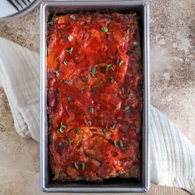 A meatloaf pan filled with Whole30 Meatloaf, sprinkled with fresh thyme on top, sitting on top of a cream colored tea towel.