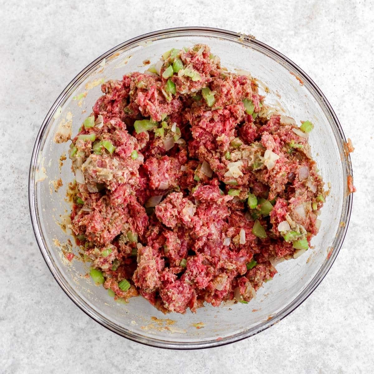A glass bowl filled with mixed up whole30 meatloaf ingredients.