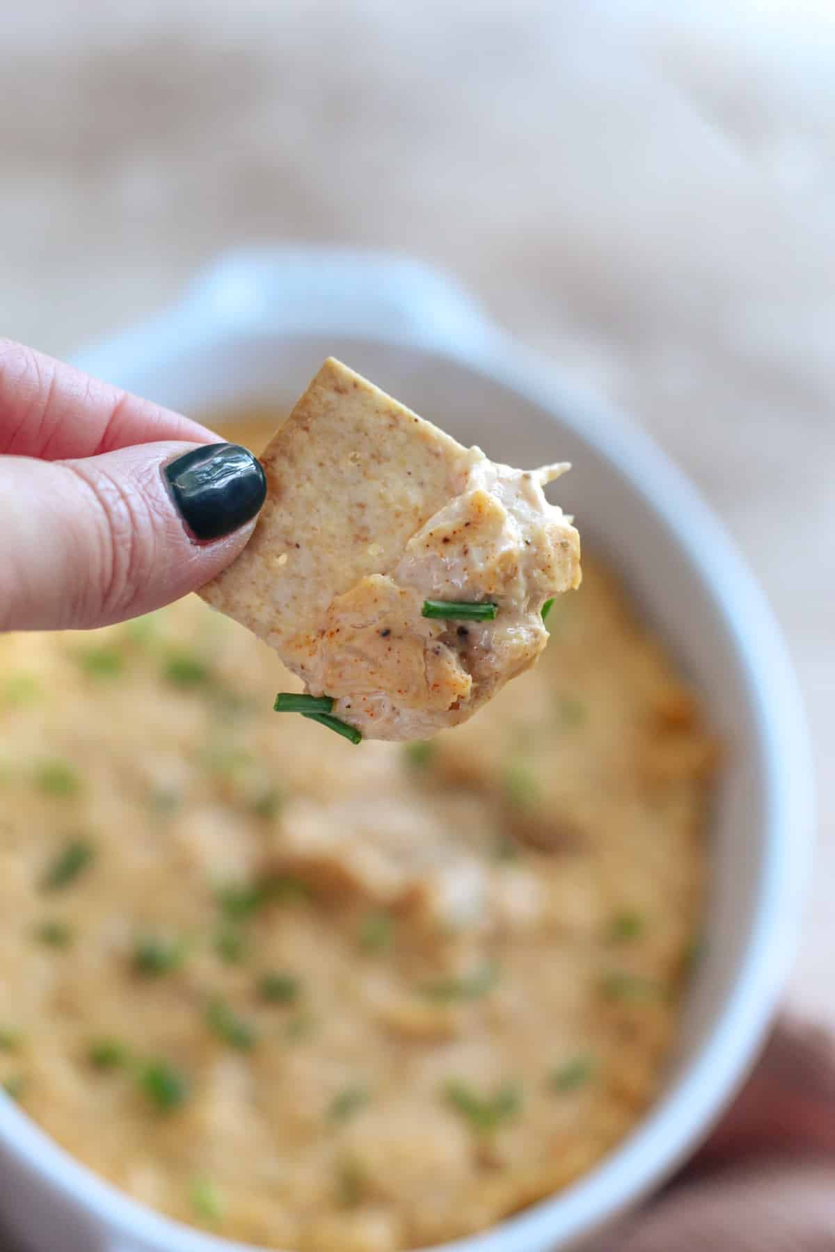 A hand holding a cracker with dairy free crab dip on the cracker.