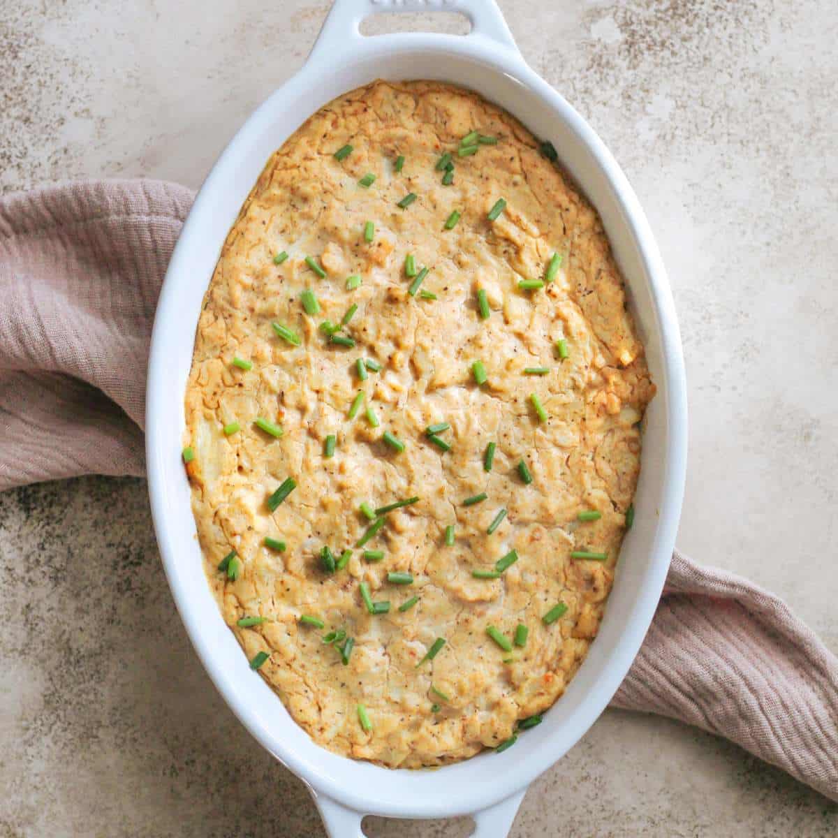 A white oval serving dish filled with dairy free crab dip sitting on a tea towel.