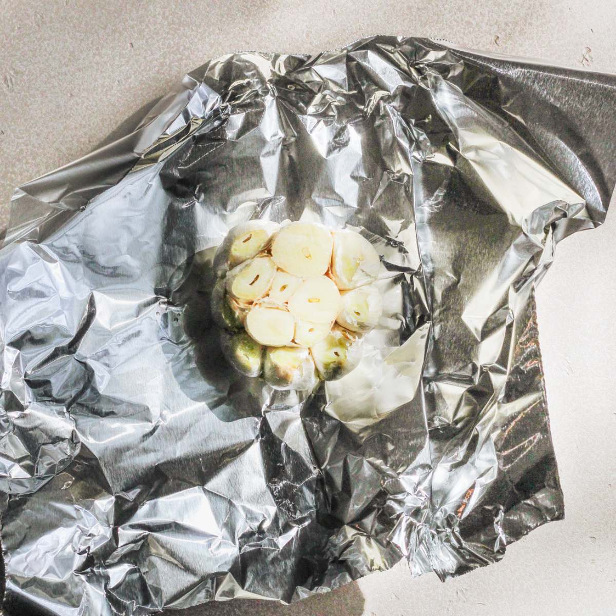 A head of garlic with the top cut off sitting on a piece of foil.