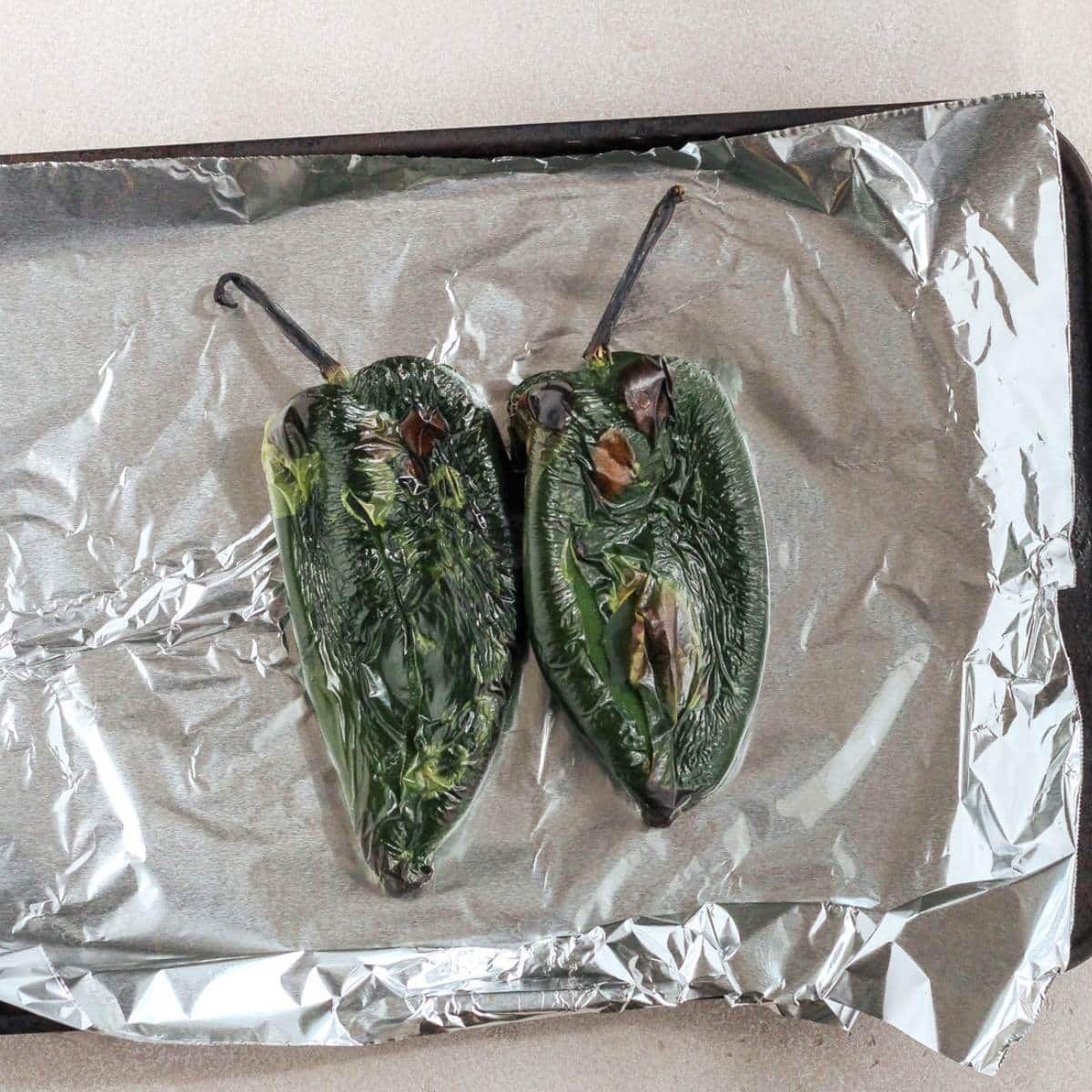Roasted poblano peppers on a sheet pan lined with foil.