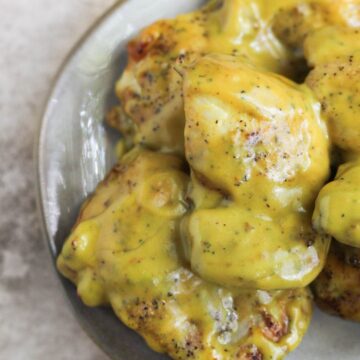 Honey mustard chicken thighs stacked on a plate.