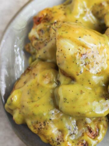 Honey mustard chicken thighs stacked on a plate.