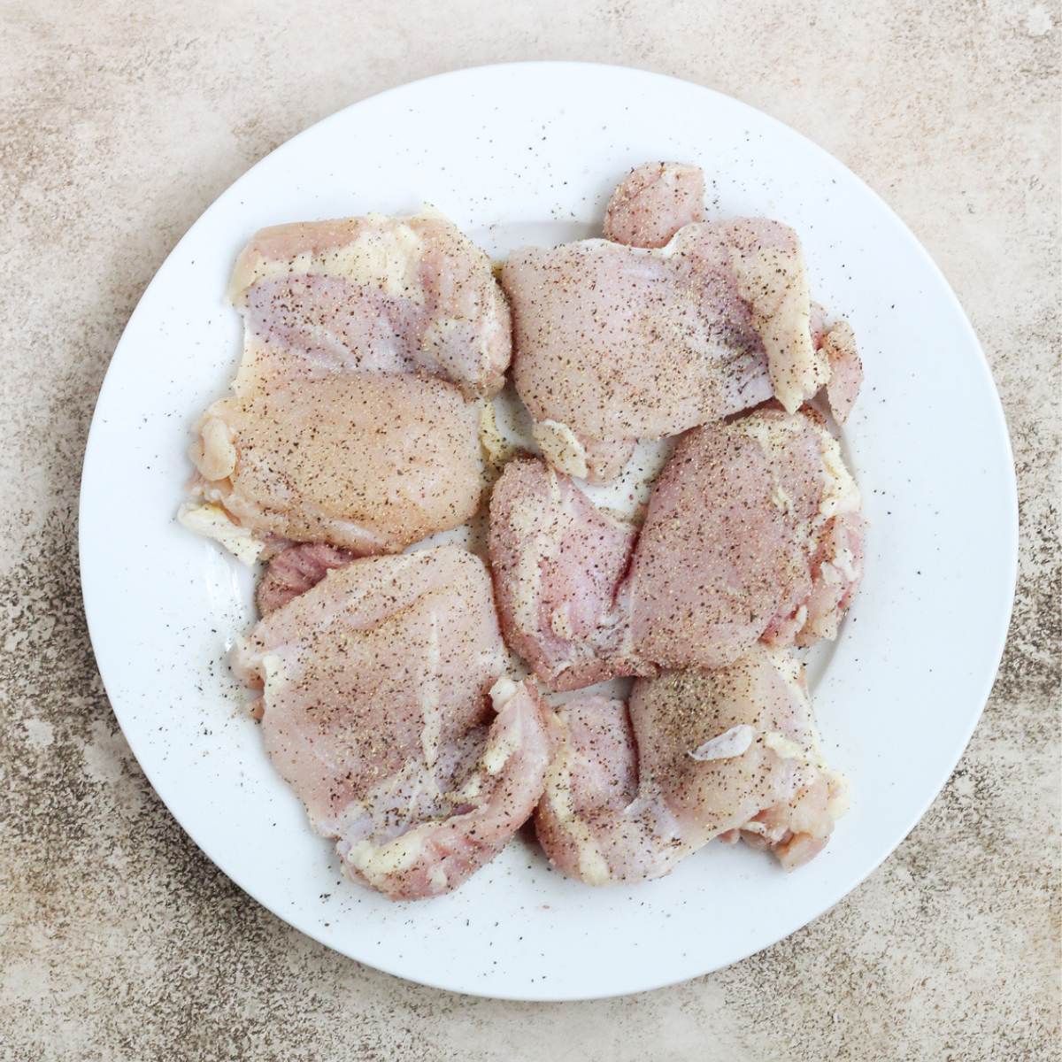 Seasoned chicken thighs on a white plate.