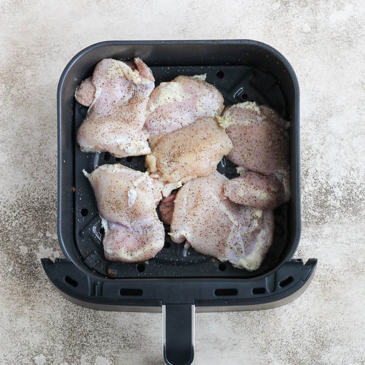 Uncooked chicken thighs in an air fryer basket.