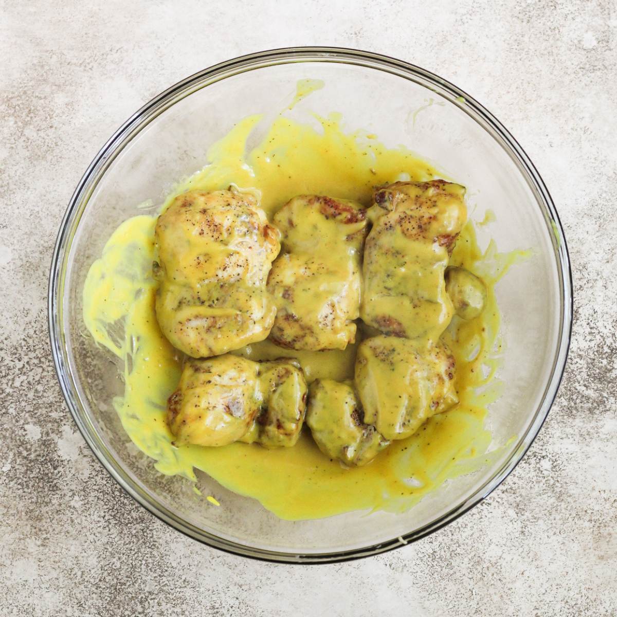 A glass bowl with honey mustard and cooked chicken thighs inside.