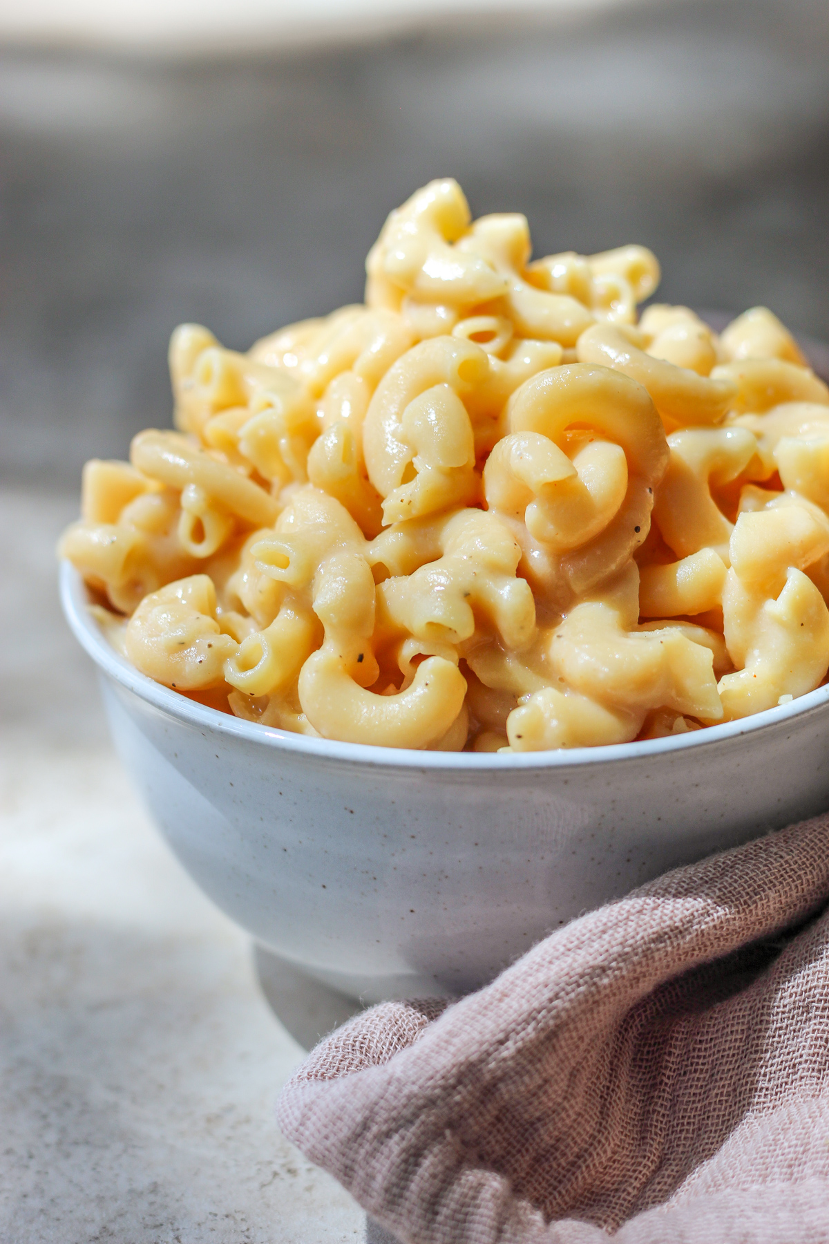 A white bowl filled with high protein mac and cheese sitting on top of a dusty pink tea towel.