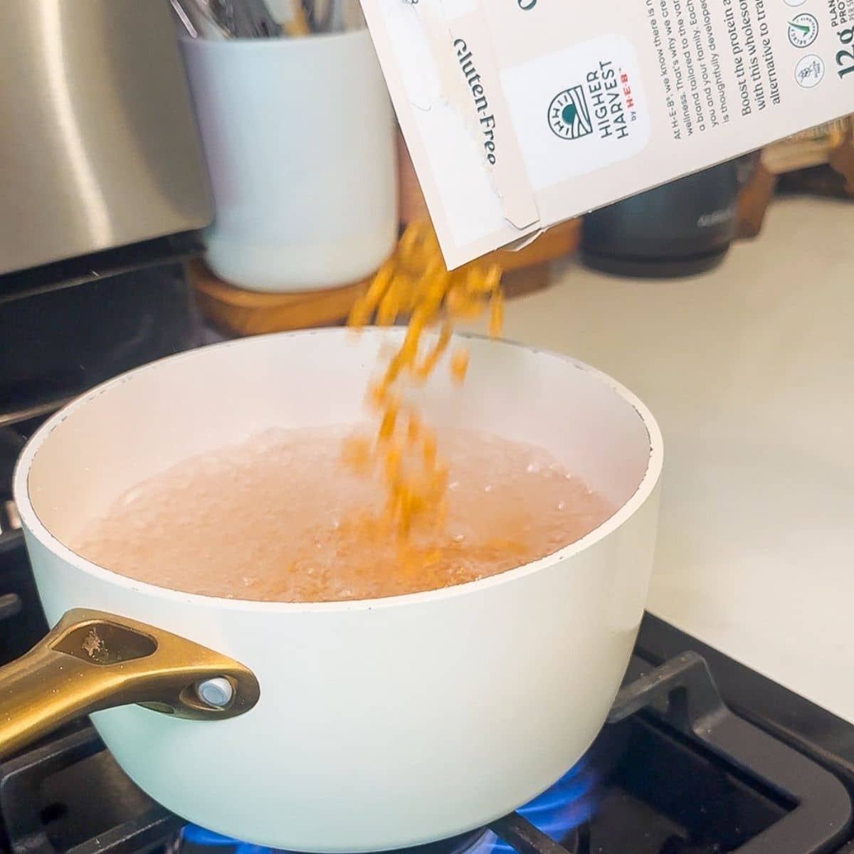 A pot of boiling water and pasta being poured in.