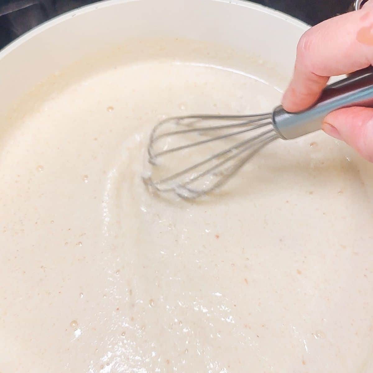 Cottage cheese sauce being whisked in a skillet.