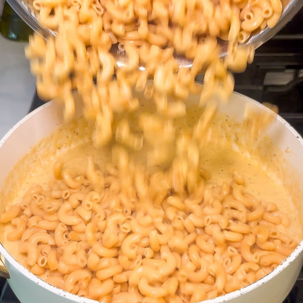 Elbow macaroni being poured into a cheese sauce.